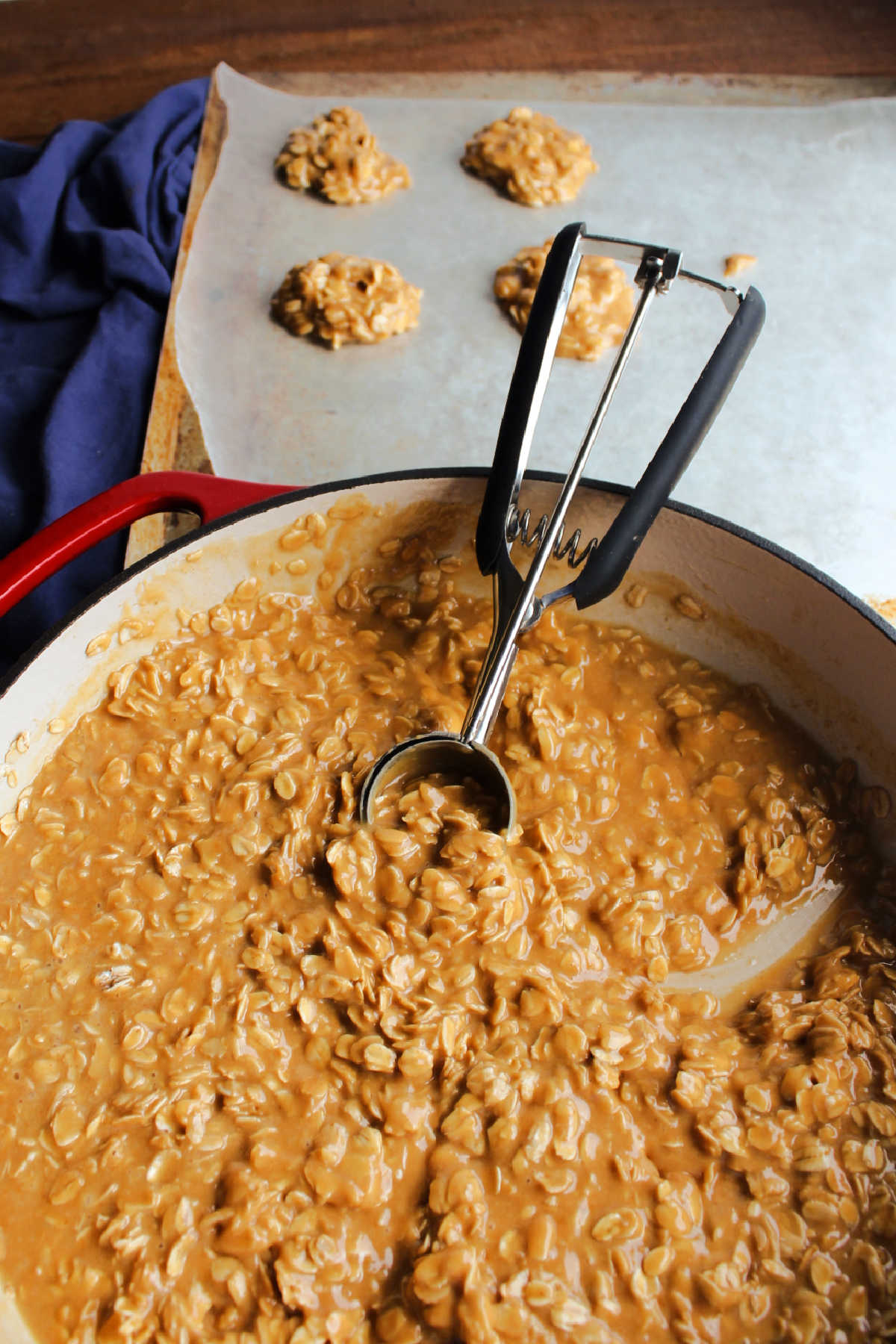 Using cookie scoop to portion out hot peanut butter and oatmeal mixture onto wax paper to form cookies.