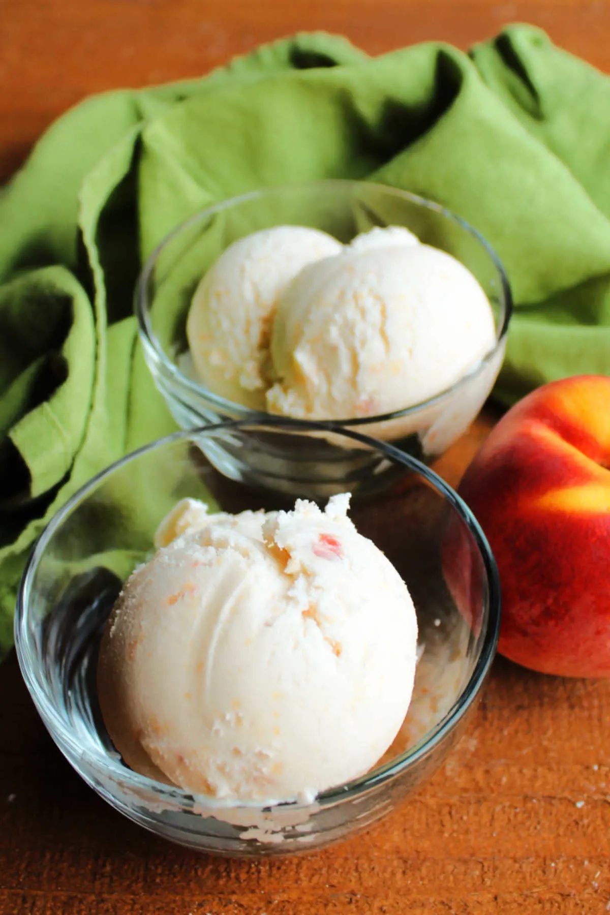Scoops of peach ice cream next to fresh peach.