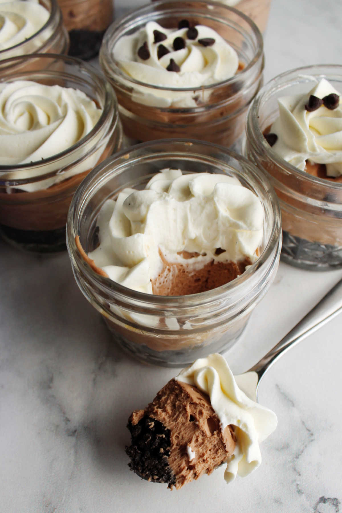 Small ball jars filled with no bake chocolate cheesecake and whipped cream with some on spoon showing layers.