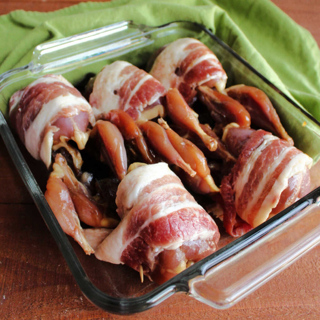 Marinated quail wrapped in bacon and in pan ready to go in oven.