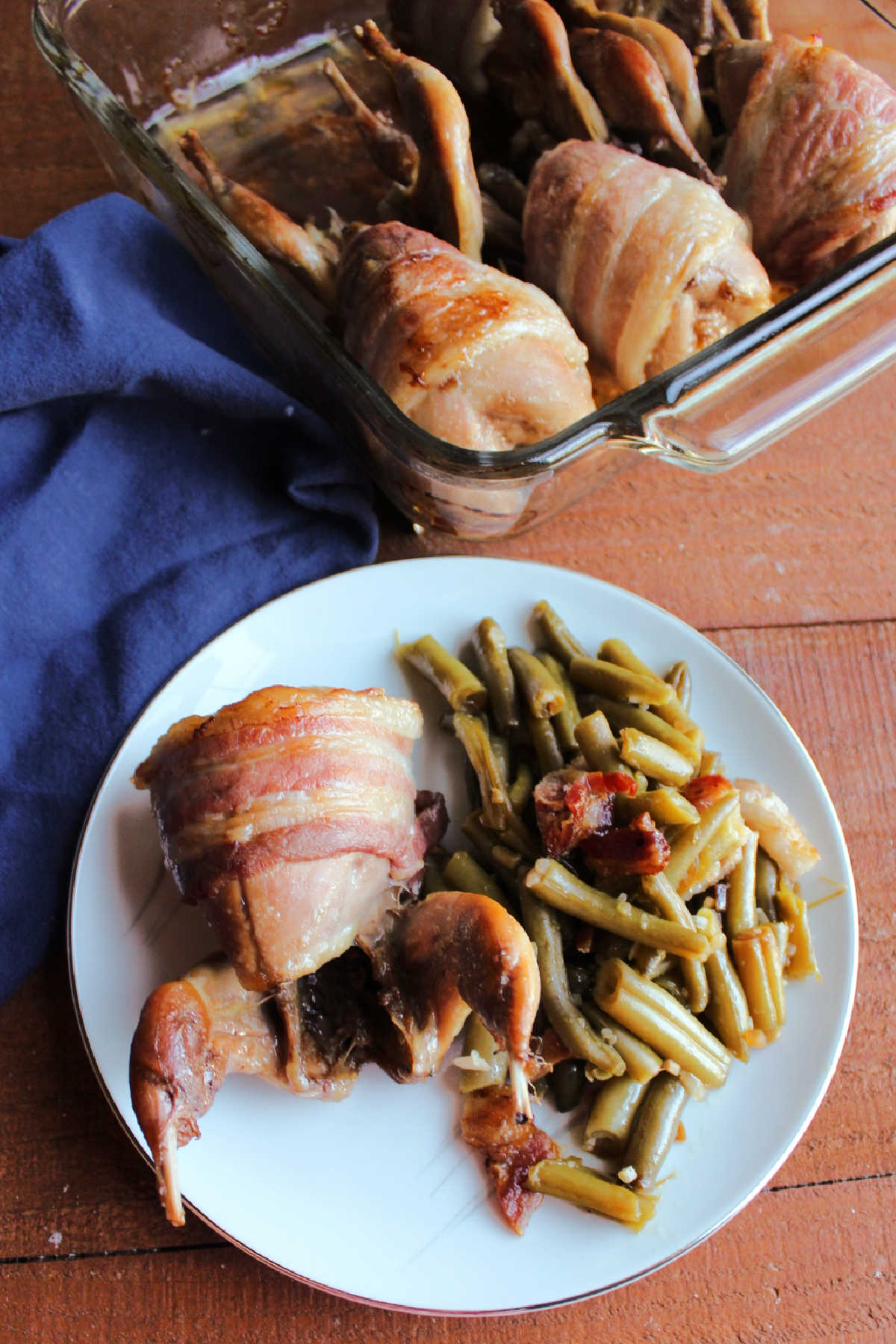 Bacon wrapped quail on plate with smothered green beans.