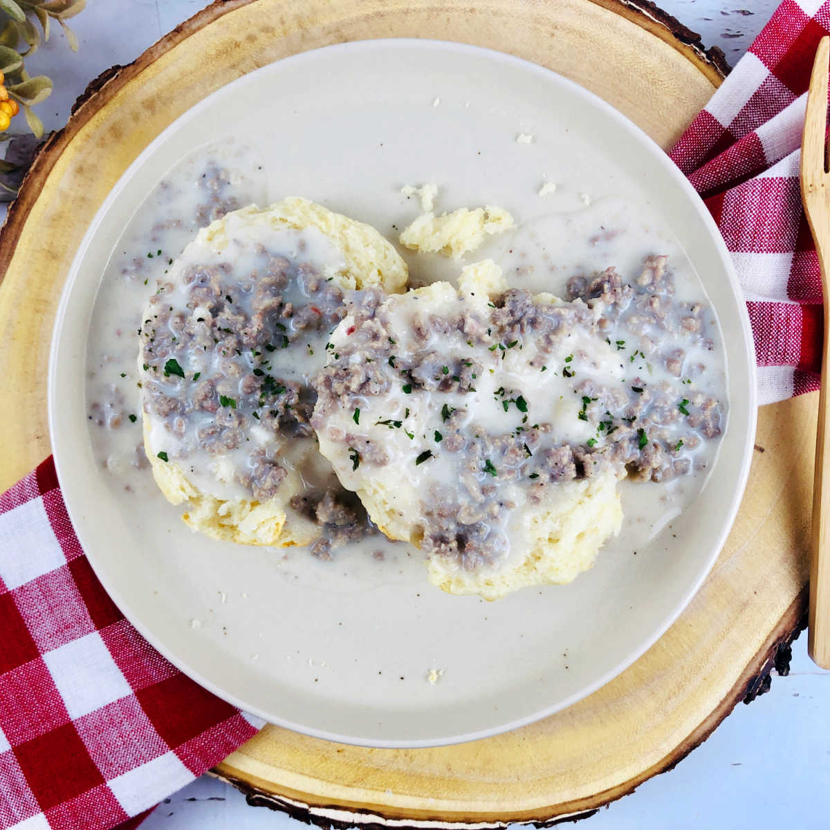 Plate of homemade biscuits topped with creamy sausage sawmill gravy with red checkered napkin.