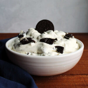 Bowl of Oreo fluff salad topped with bits of cookies and one whole chocolate cookie on top.