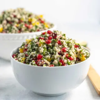 Bowl of pomegranate couscous salad with fresh herbs, bright pomegranate arils and bits of yellow bell pepper, ready to eat.