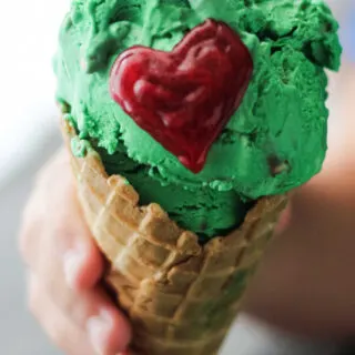 Child's hand holding ice cream cone filled with green ice cream with red heart to look like the Grinch.