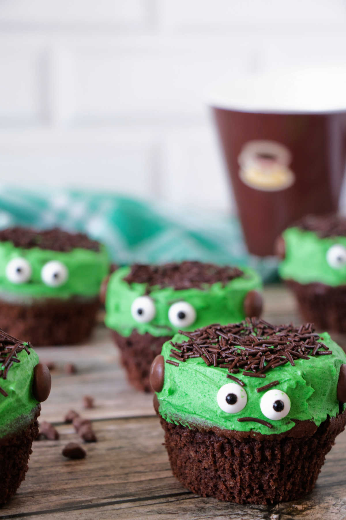 Lots of Frankenstein cupcakes in front of coffee cup.
