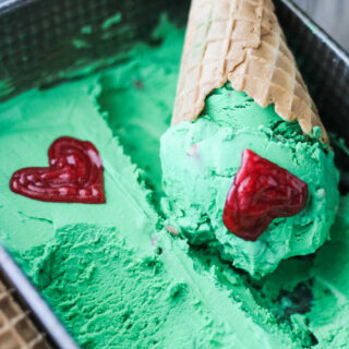 cone of green grinch ice cream with red icing hearts.