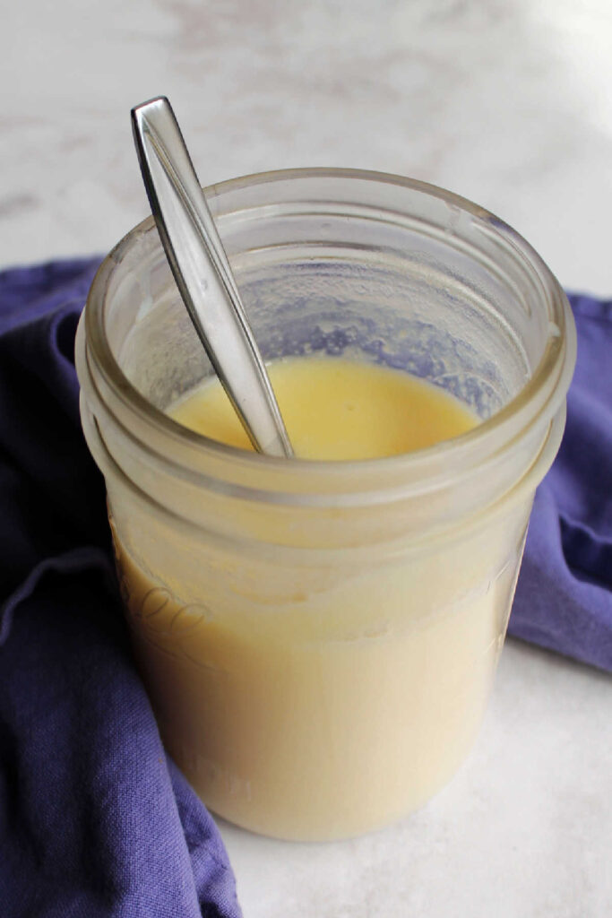 Pale yellow sweetened condensed milk and spoon in jar.
