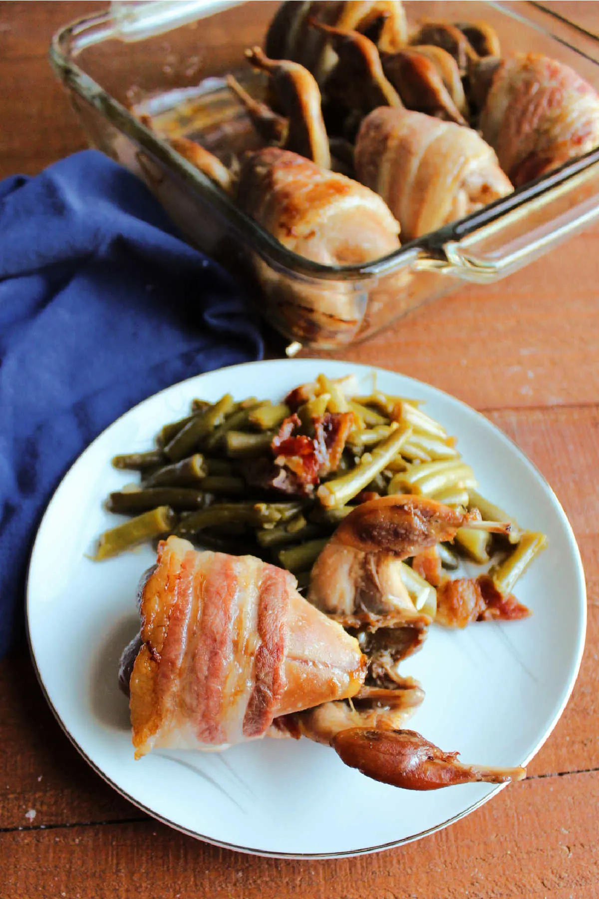 Quail and green beans on plate with pan full of quail in background.