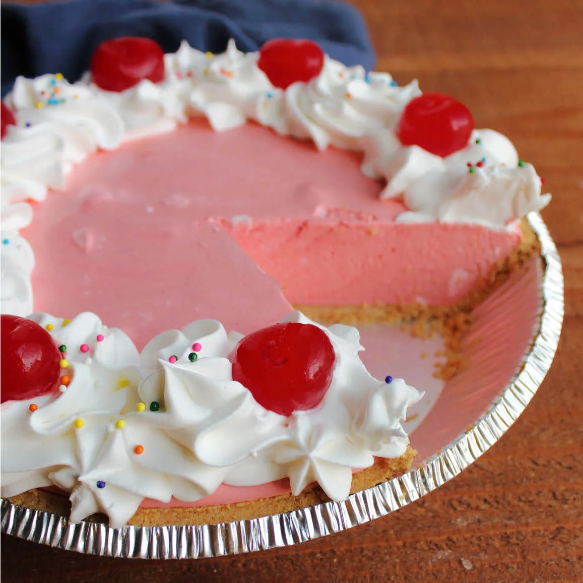 Pie plate with pink jello pie inside with a piece missing.