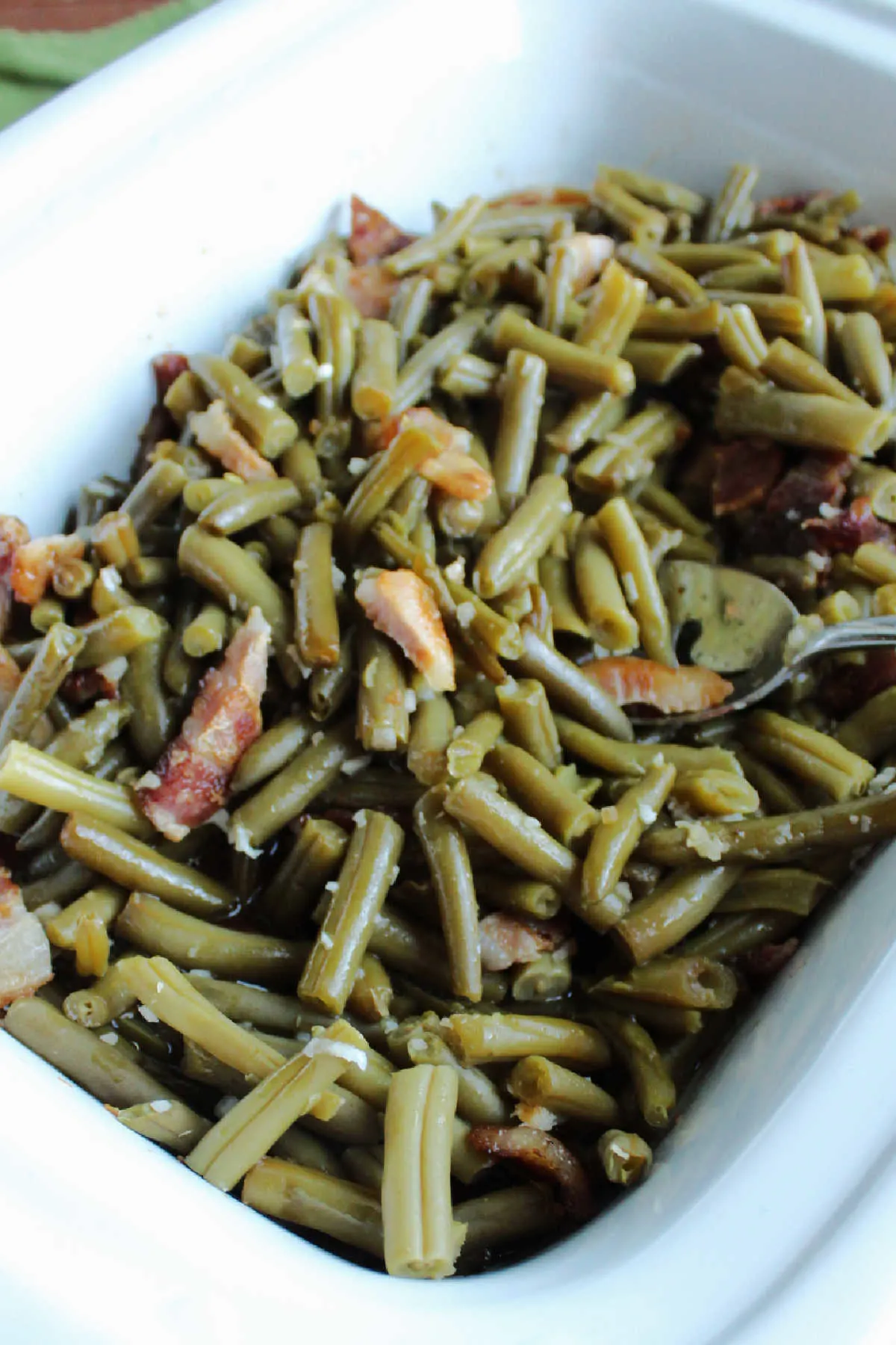 Slow cooker filled with sweet and sour green beans and bacon ready to serve. 