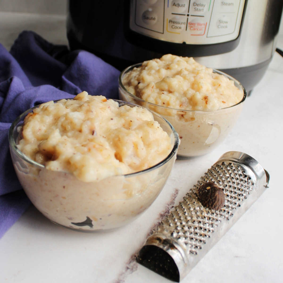 Two glass bowls of rice pudding next to nutmeg grater in front of instant pot.