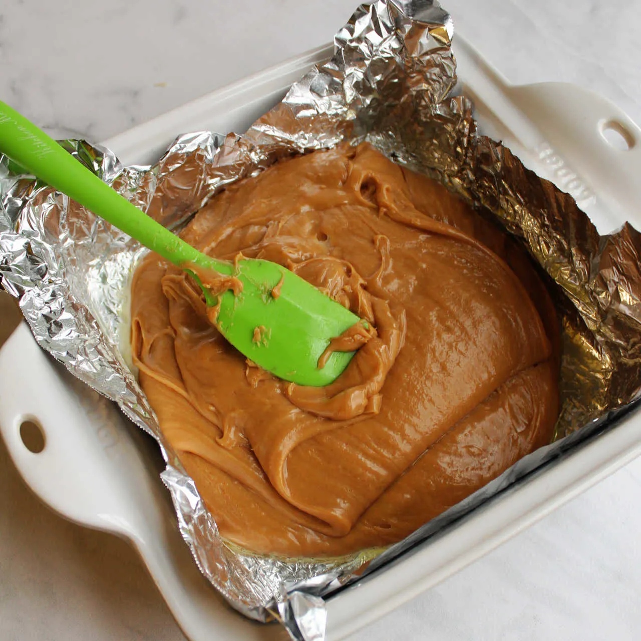 Spreading peanut butter fudge mixture into foil lined pan.
