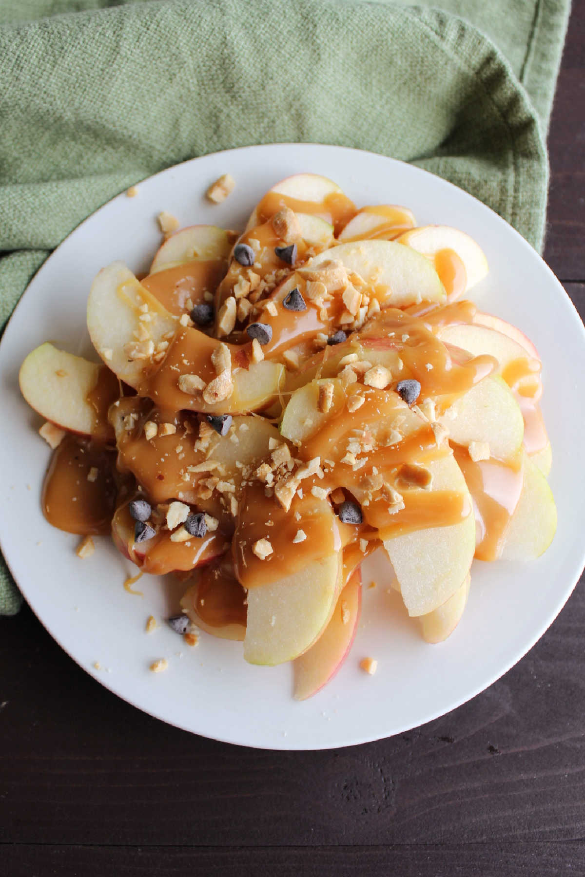 Plate of apple slices topped with caramel sauce, mini chocolate chips and chopped peanuts to make apple nachos.