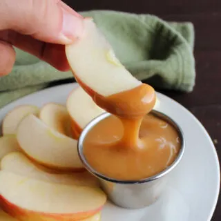 Apple slice dipped into container of homemade caramel sauce.