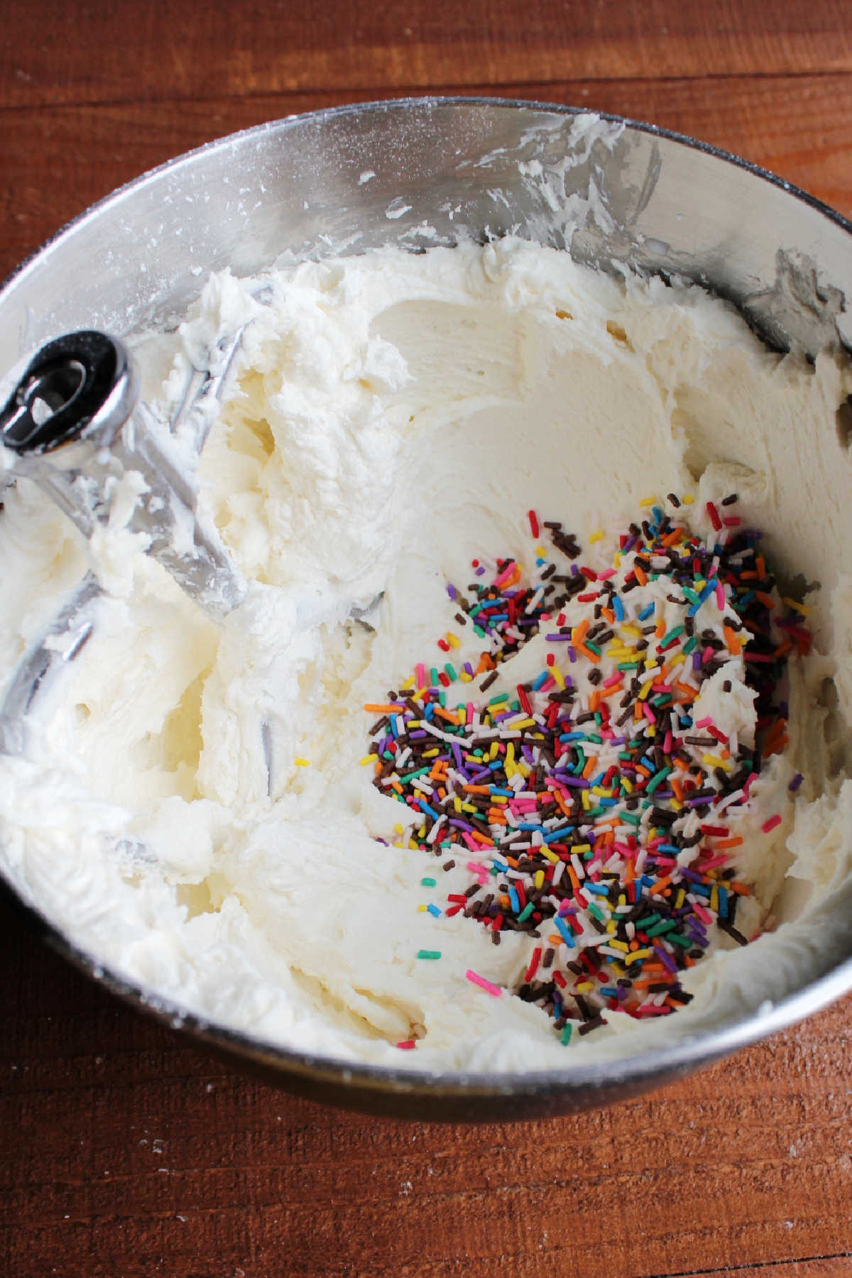 Bowl of buttercream with pile of sprinkles inside, ready to be mixed together.