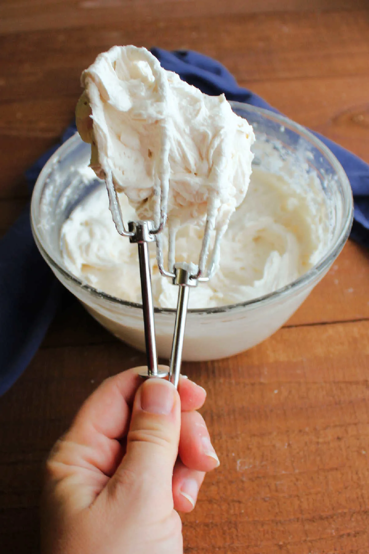 Hand holding mixer beaters filled with cinnamon buttercream. 