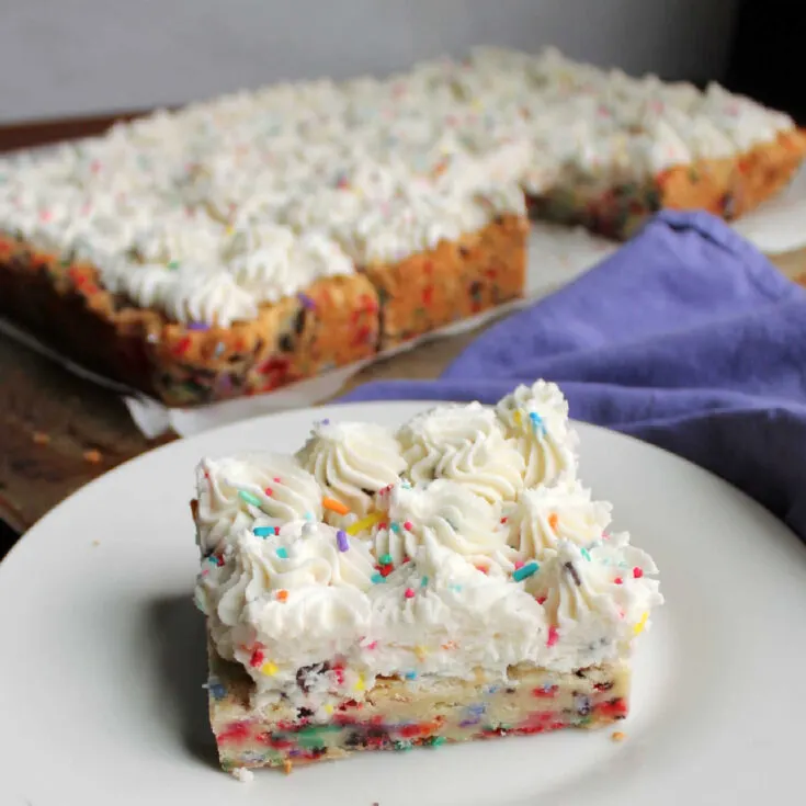 Funfetti sugar cookie bar with swirls of frosting on plate ready to eat.