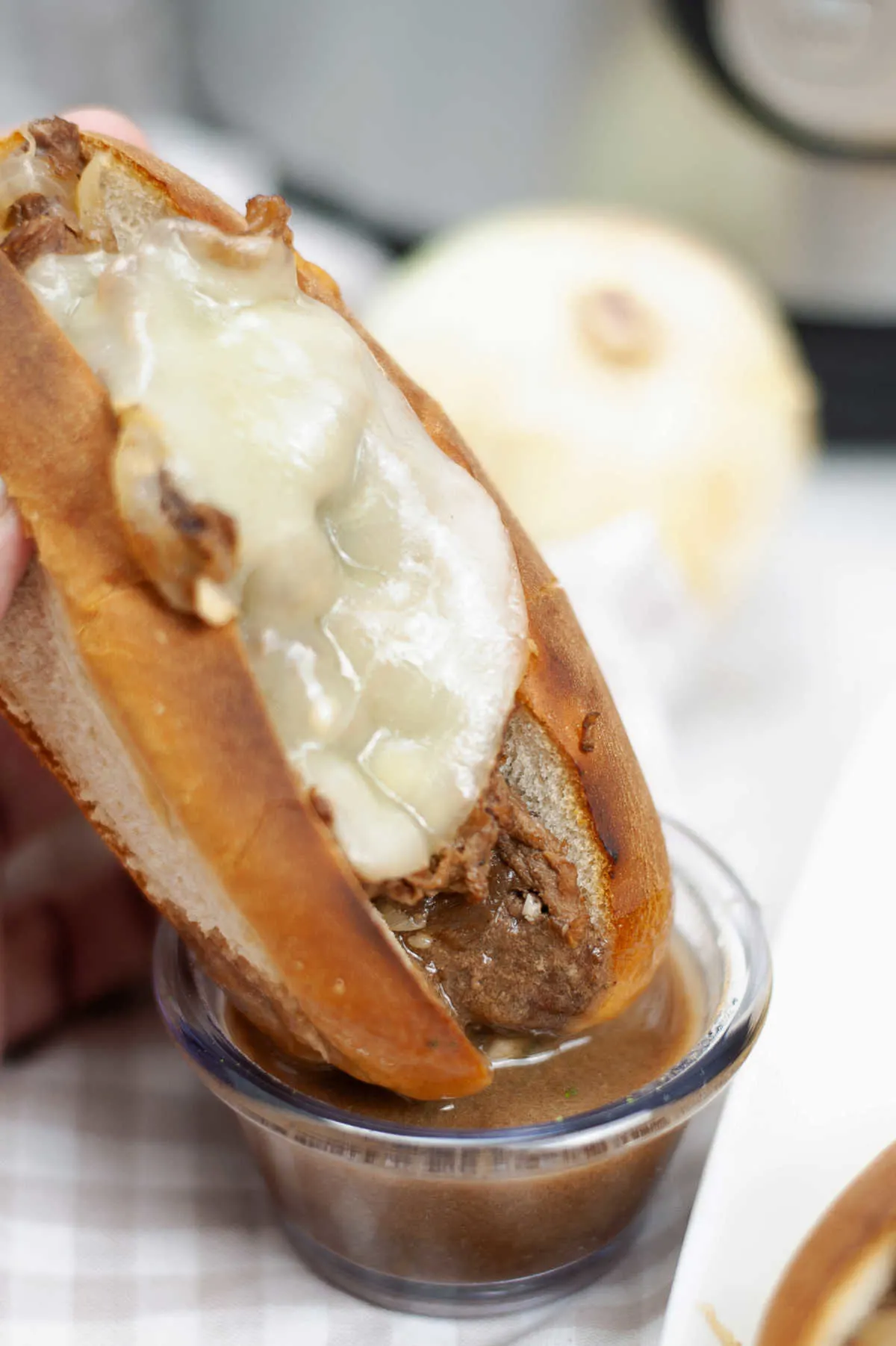 Dipping french dip sandwich with melted cheese into small bowl of au jous.