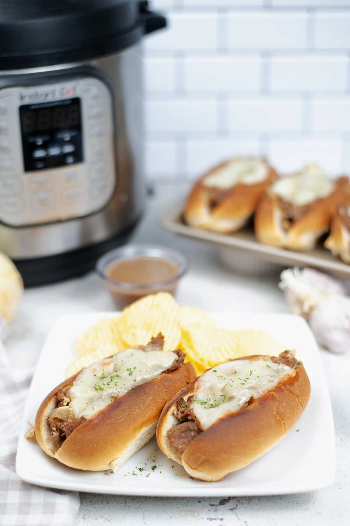 Plate of french dip sandwiches and potato chips in front of instant pot.