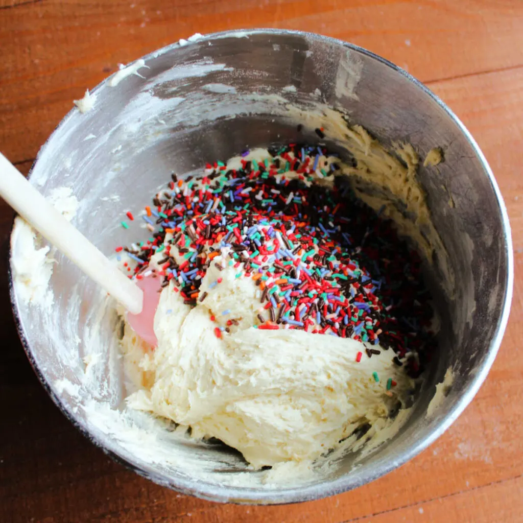 Sugar cookie dough and lots of sprinkles in mixing bowl ready to be mixed together. 