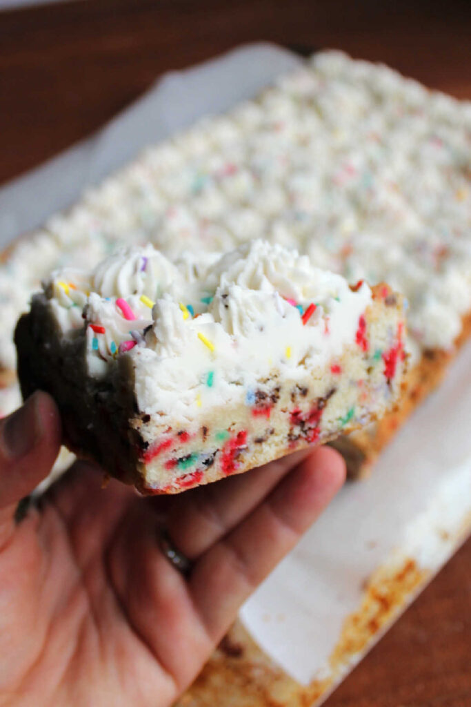 Hand holding a soft sugar cookie bar filled with colorful sprinkles.