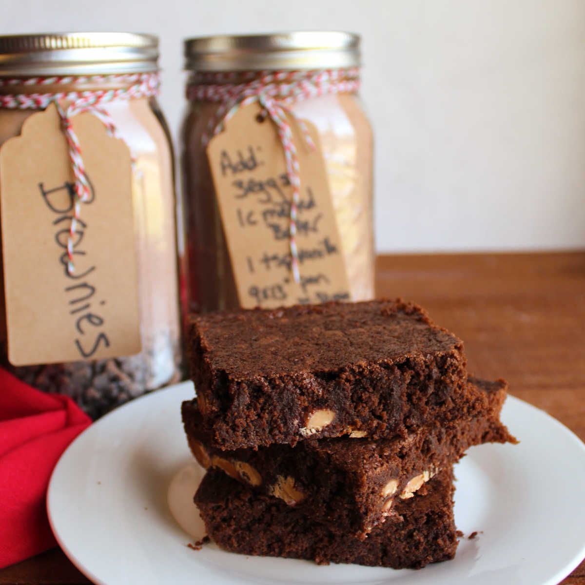 Stack of homemade brownies in front of jars filled with brownie mix.