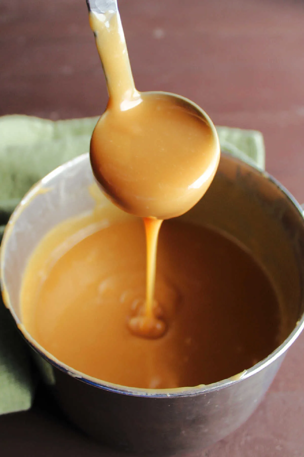 Ladle filled with thick rich caramel sauce with some dripping over the edge into the saucepan.