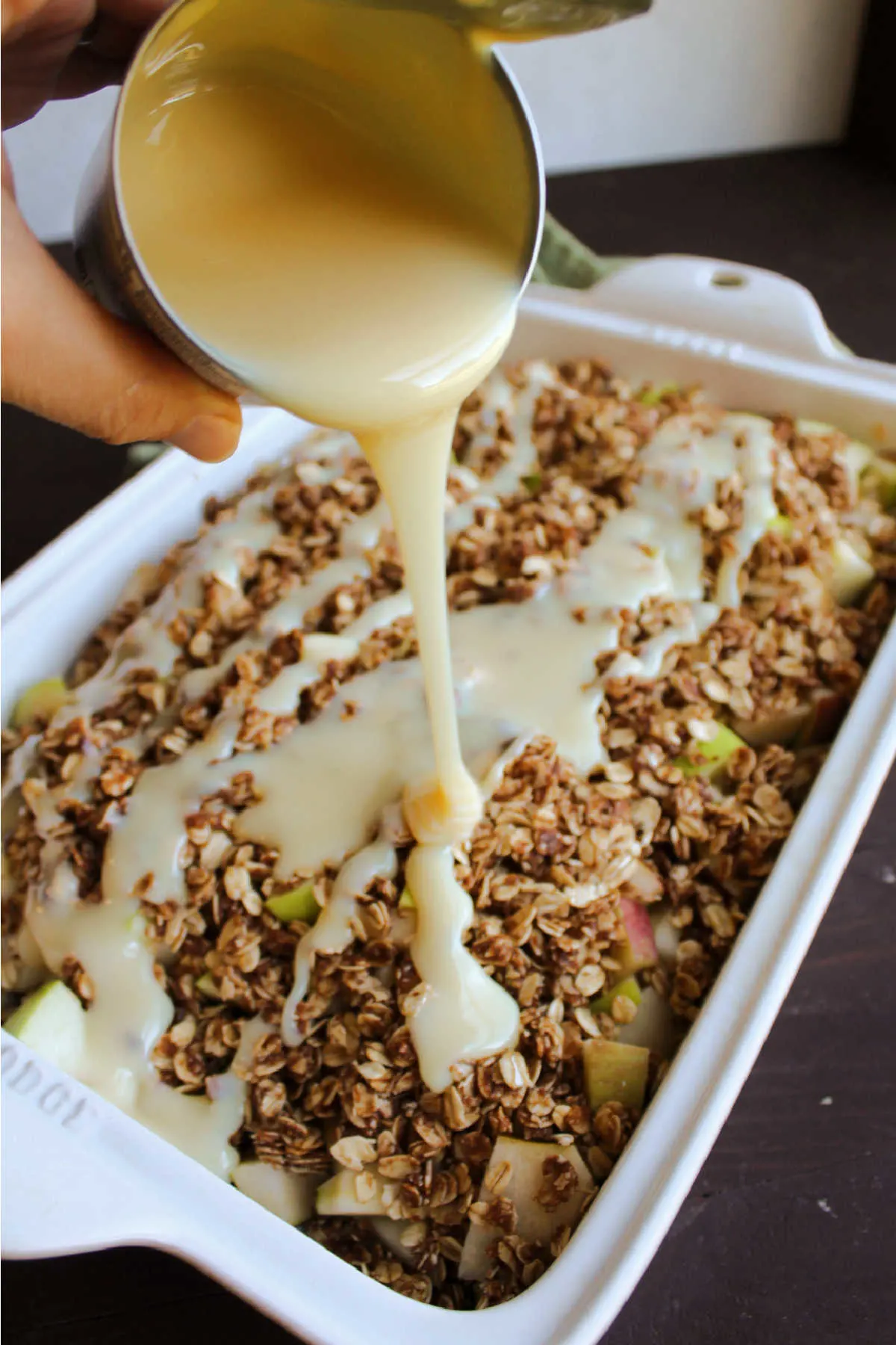 Pouring a can of sweetened condensed milk over apple crisp before it goes in the oven.
