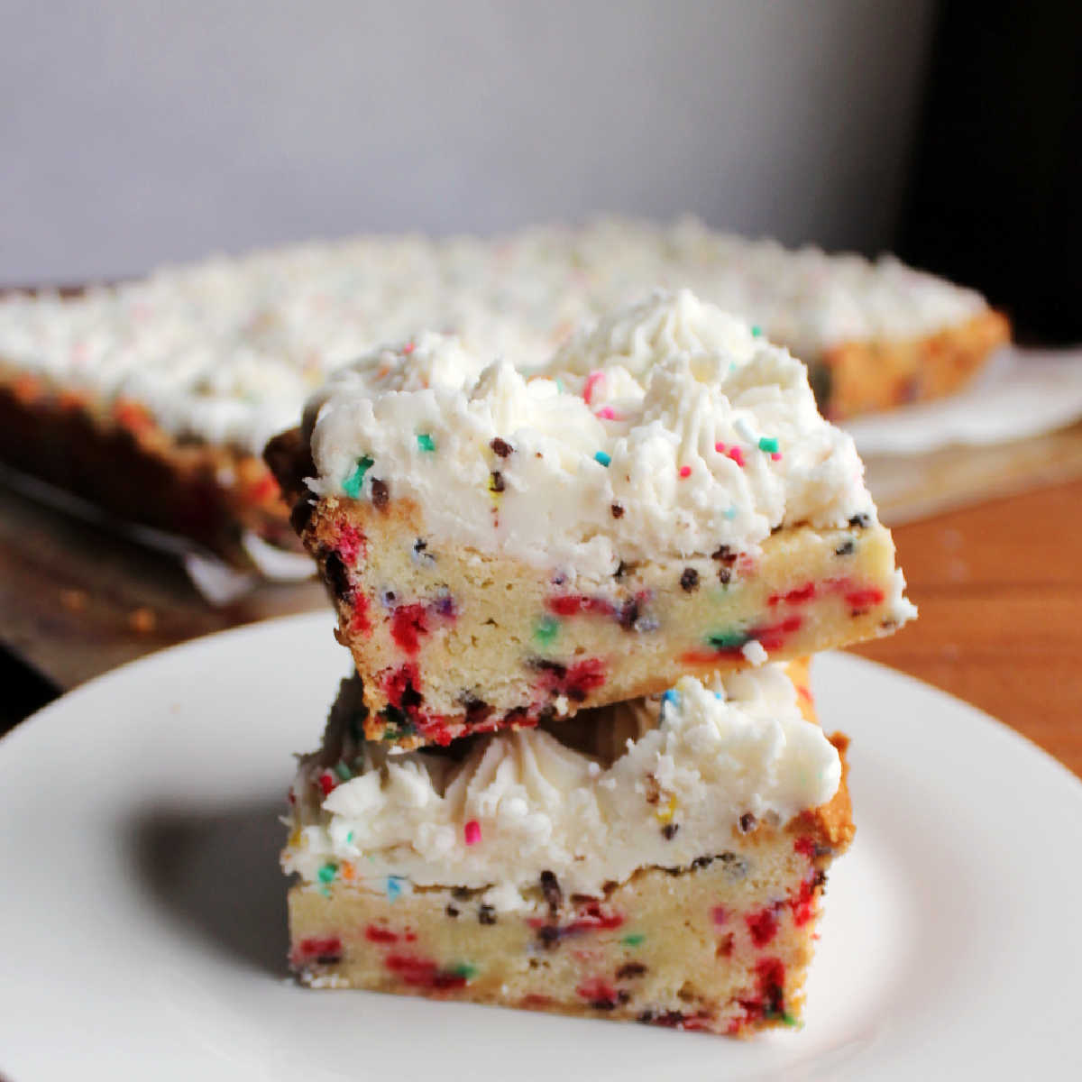 Two thick soft frosted sugar cookie bars with lots of sprinkles stacked on top of each other.