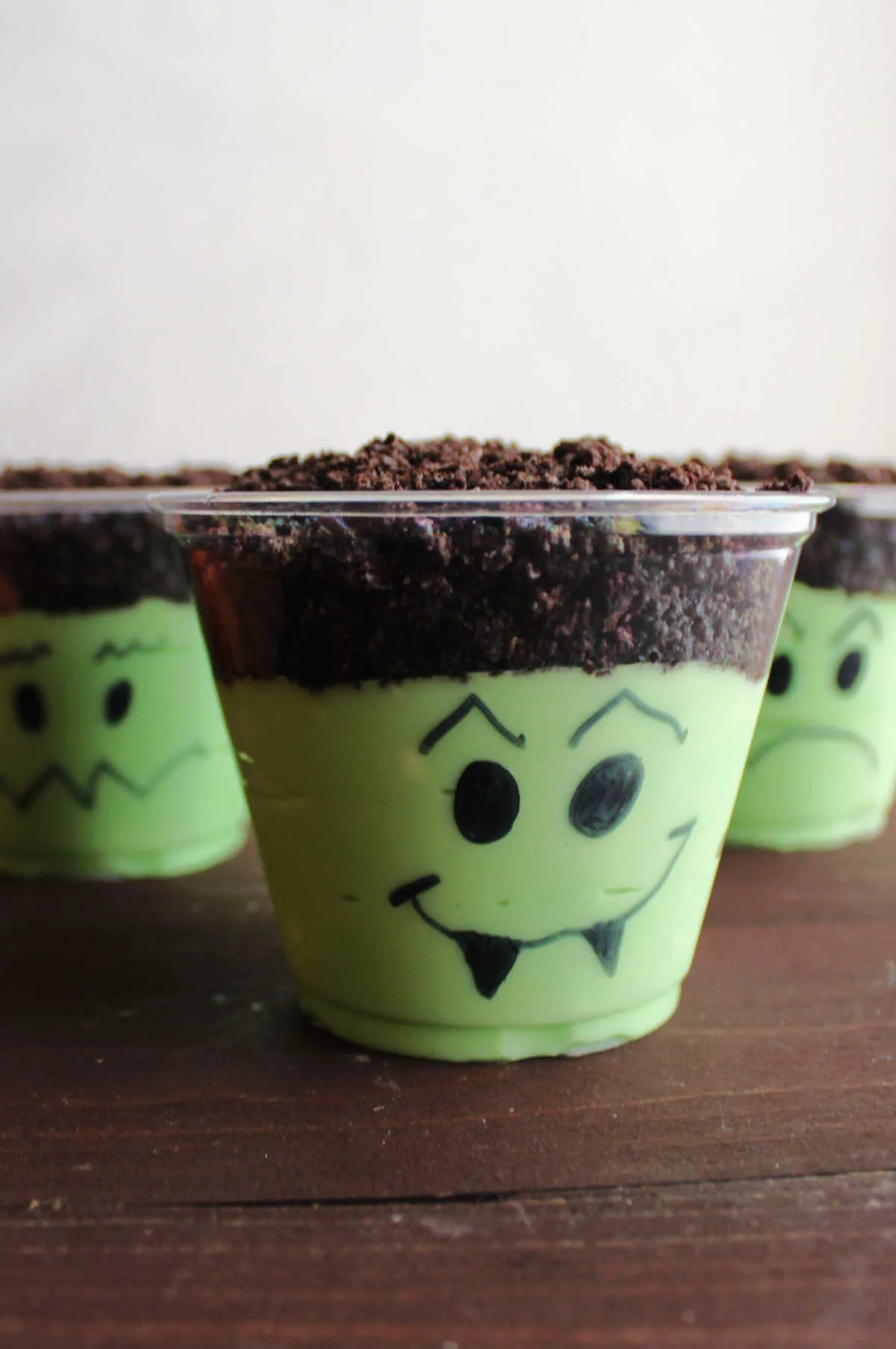 Green dirt pudding cups with Halloween faces drawn on them, ready to eat. 
