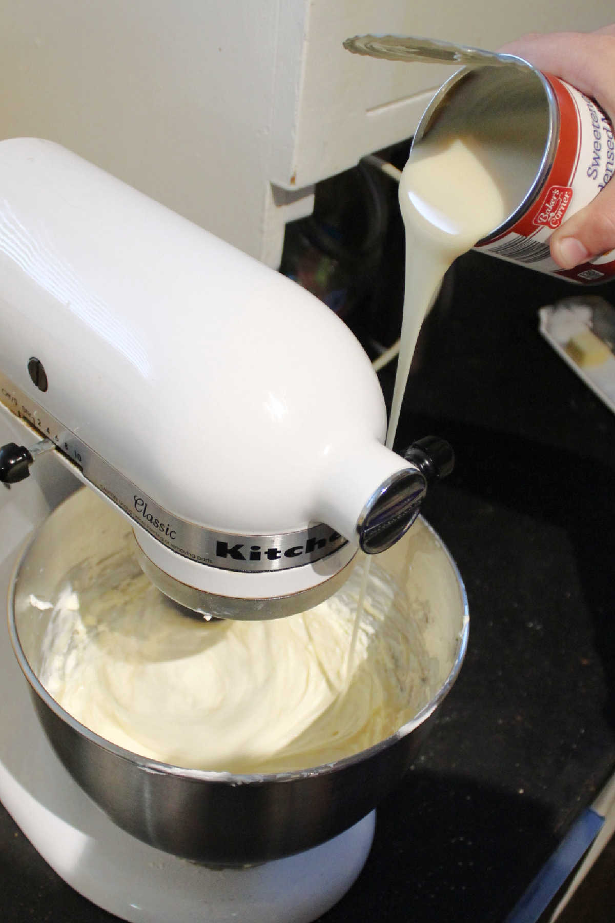 Slowing pouring sweetened condensed milk into beaten cream cheese. 