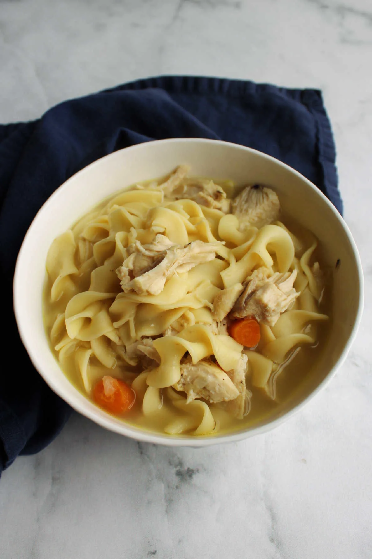 Bowl of homemade chicken noodle soup with wide egg noodles, chunks of carrot and chicken.