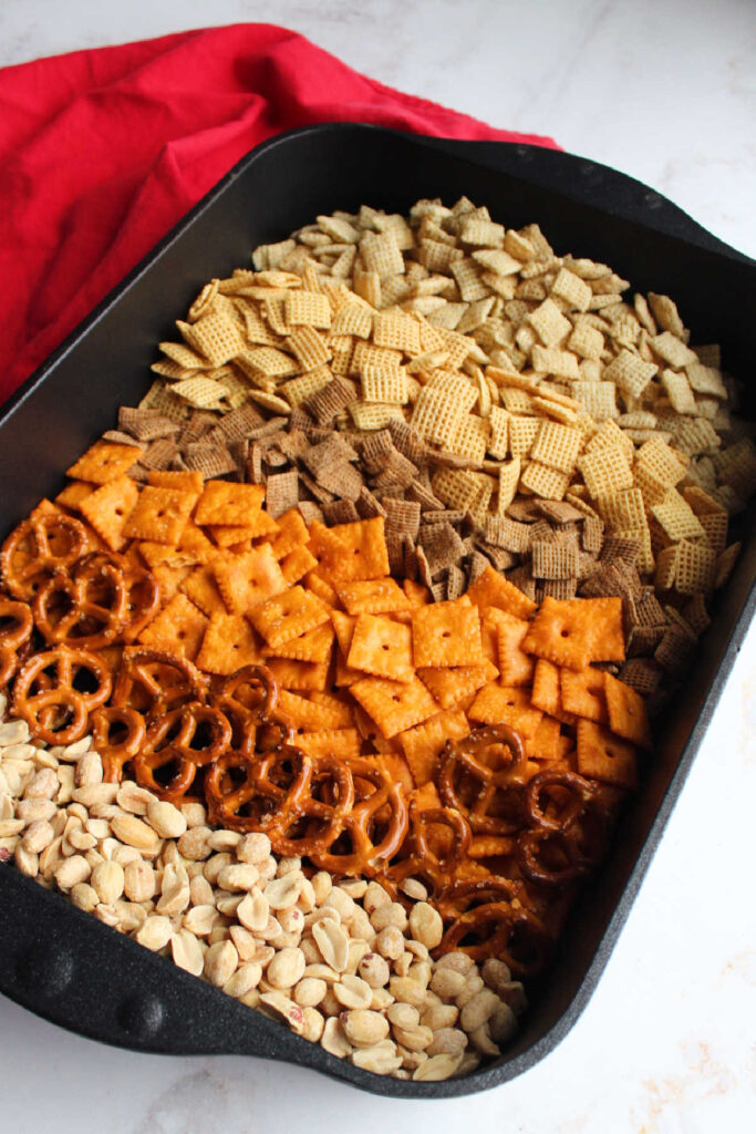 Roasting pan filled with different cereals, cheese crackers, pretzels and peanuts ready to be made into chex mix.