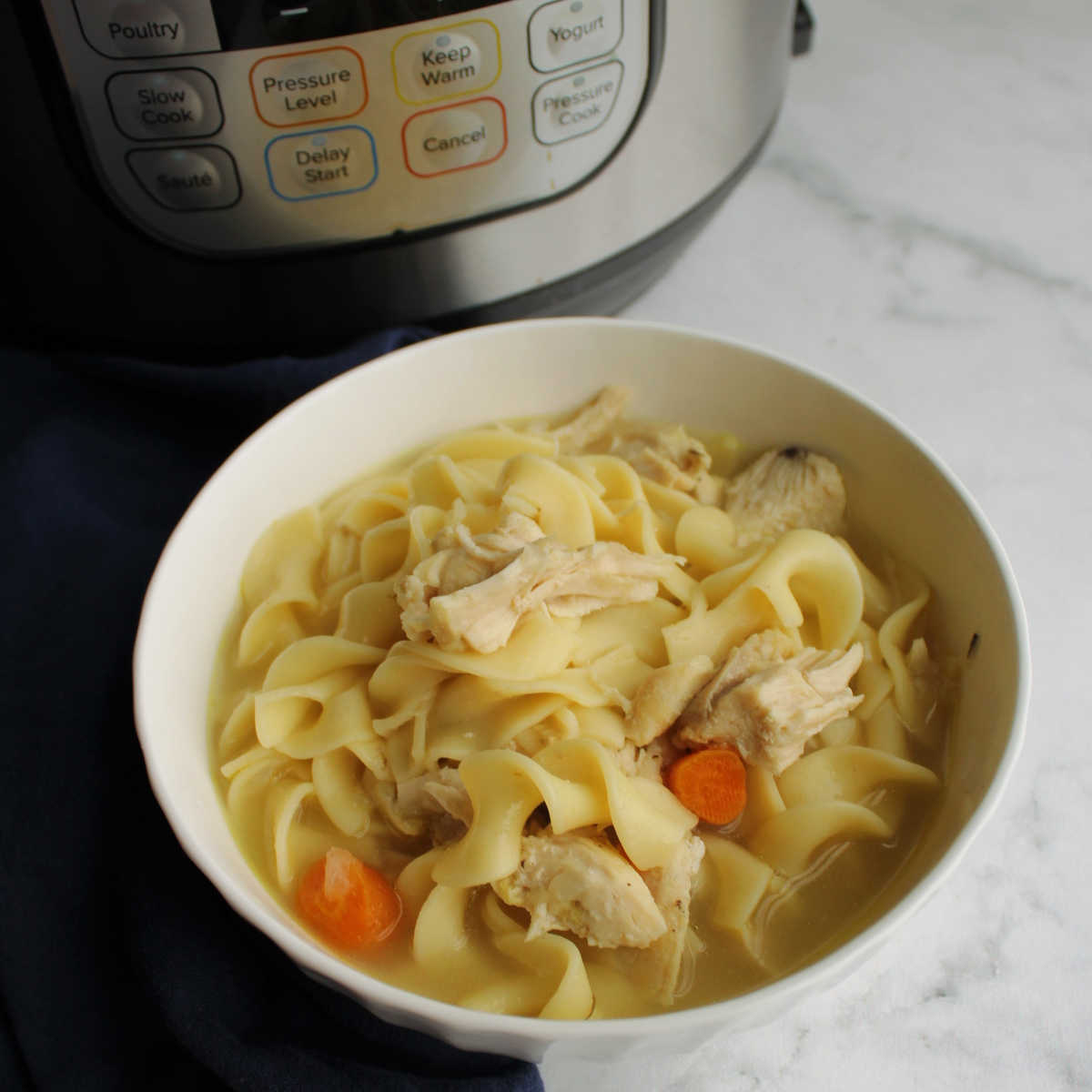 Bowl of homemade chicken noodle soup in front of instant pot.