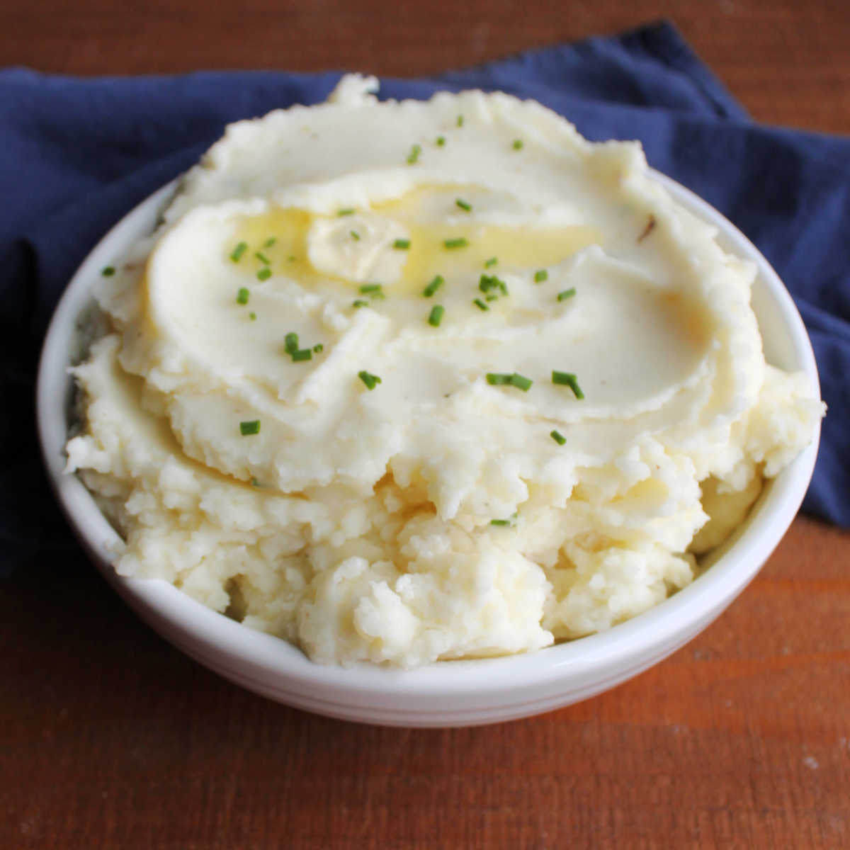 Serving bowl filled with cream sour cream and chive mashed potatoes topped with extra melted butter and bits of fresh green chive.