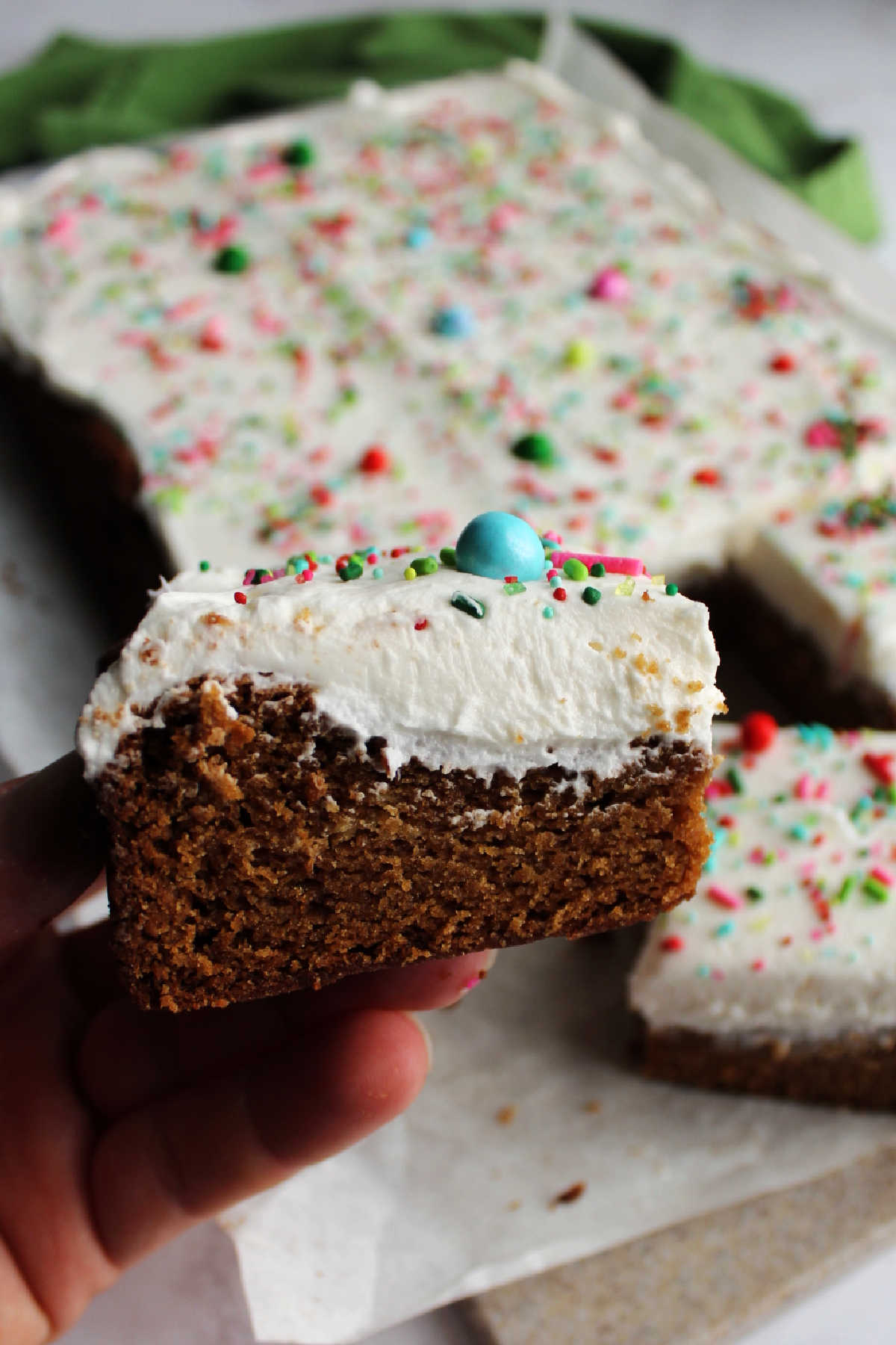 Hand holding a thick gingerbread cookie bar with soft cookie and fluffy buttercream. 
