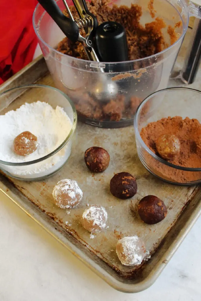 Rolling small bourbon balls in a bowl of powdered sugar and a bowl of cocoa powder.