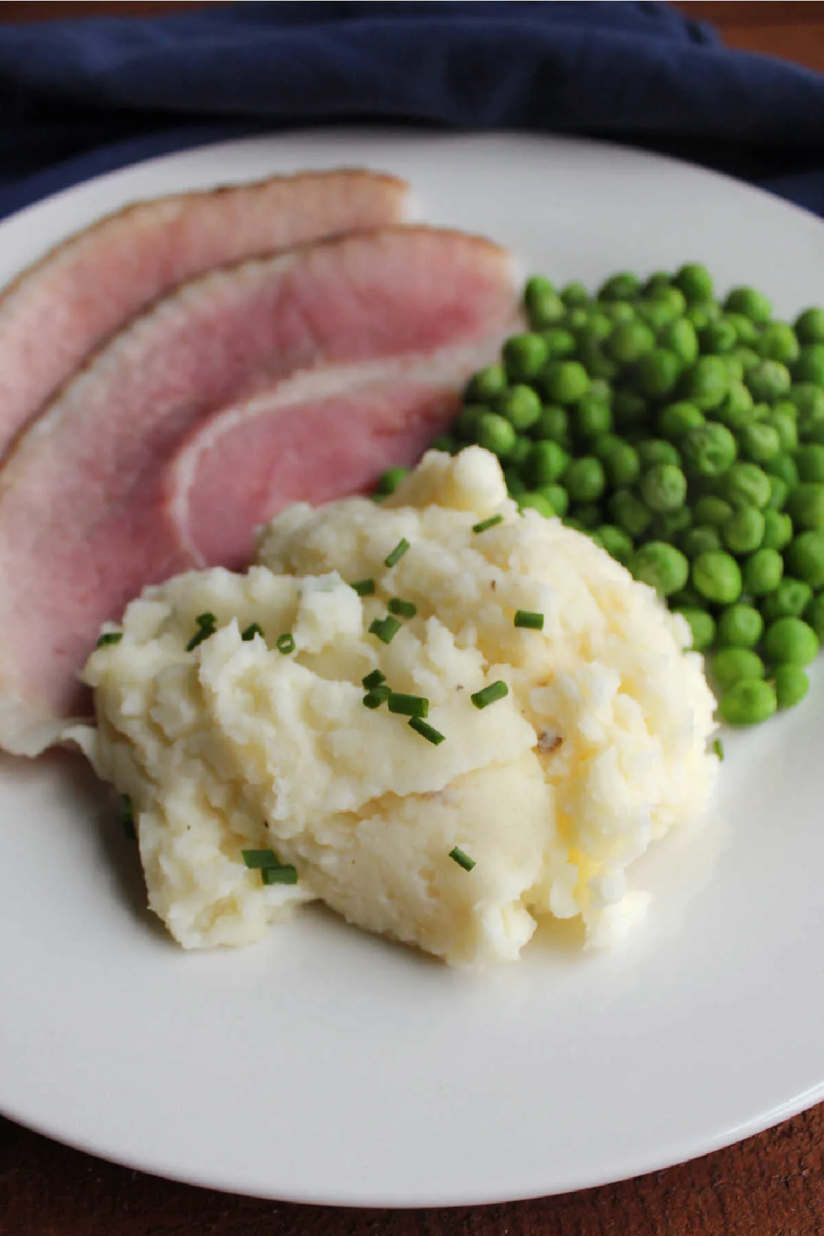Plate of sour cream and chive mashed potatoes, slices of ham and peas.