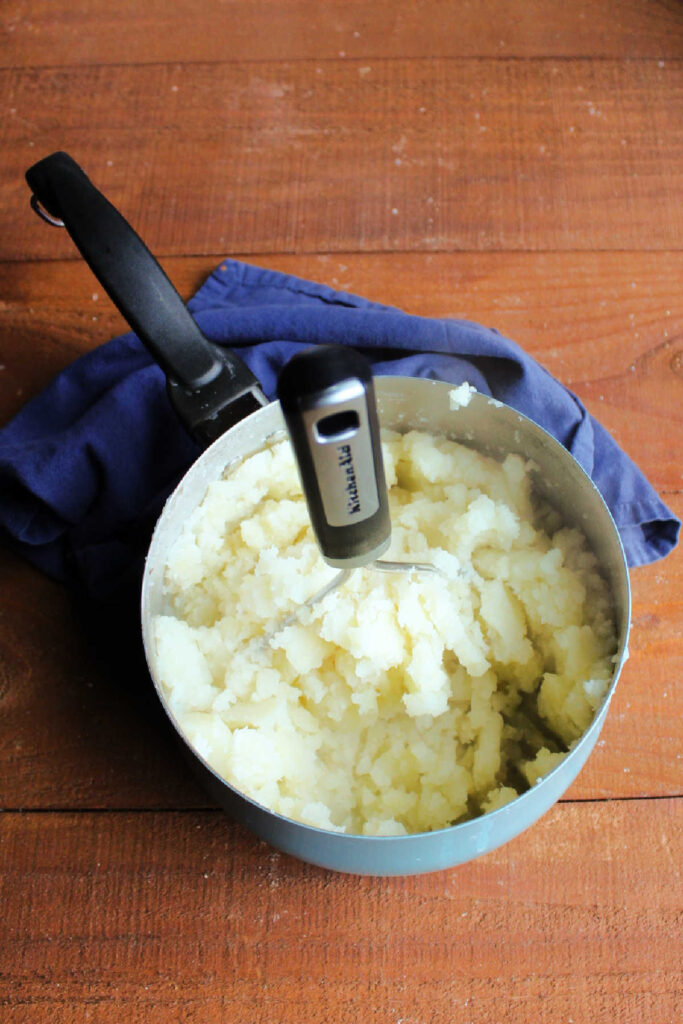 Potato masher mashing cooked and drained potatoes.