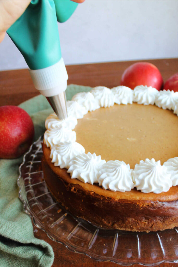 Piping cream cheese whipped cream border on chilled apple butter cheesecake.