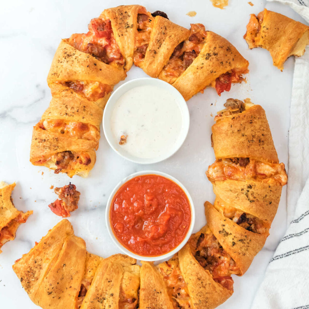 Pizza crescent ring served with a bowl of ranch and a bowl of marinara ready to eat. 