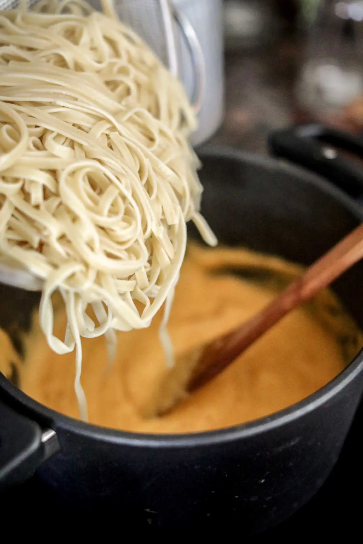 Pouring drained pasta into prepared butternut alfredo sauce. 