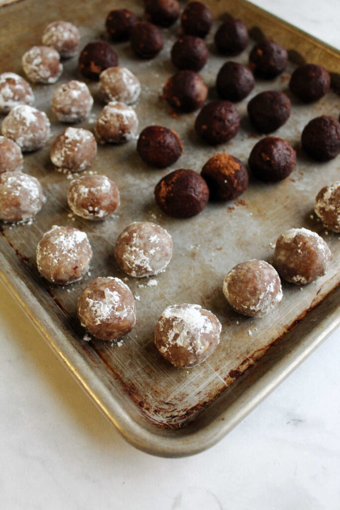 Tray of freshly made bourbon balls, some rolled in powdered sugar and some rolled in cocoa powder.