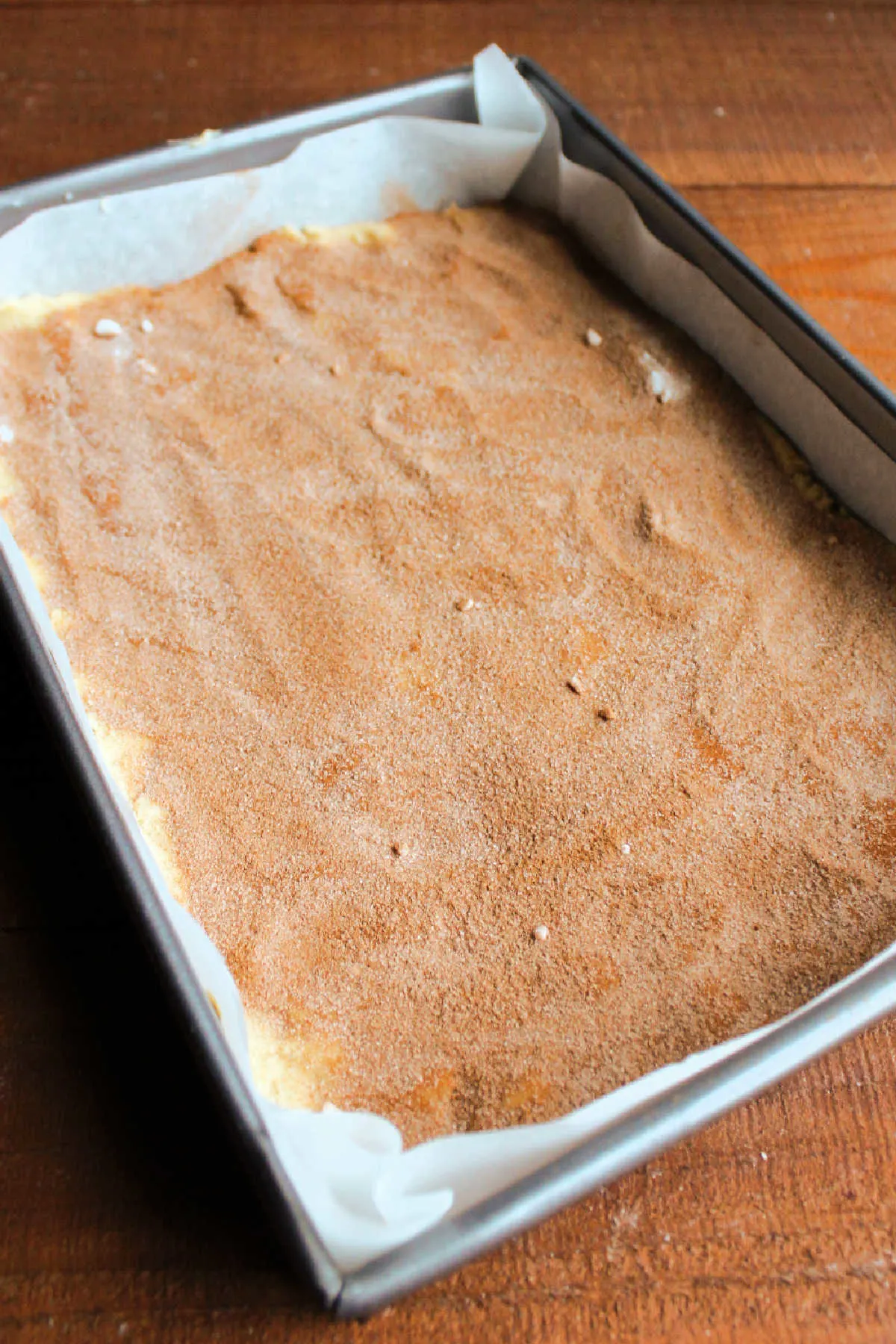 9x13-inch pan lined with parchment paper and filled with cinnamon sugar topped snickerdoodle dough, ready to bake.