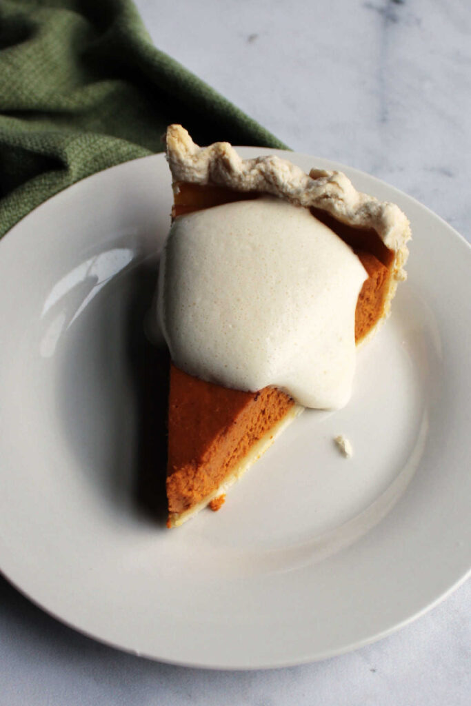 Soft evaporated milk whipped cream on top of a slice of maple pumpkin pie.