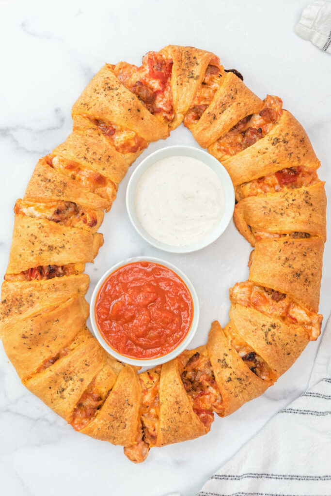 Freshly baked pizza pull apart wreath with a bowl of marinara sauce and a bowl of ranch in the middle ready to serve. 