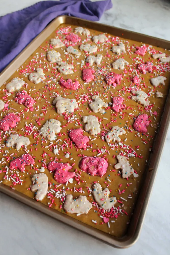 Pan of blondie batter topped with circus animal cookies and sprinkles ready to bake.