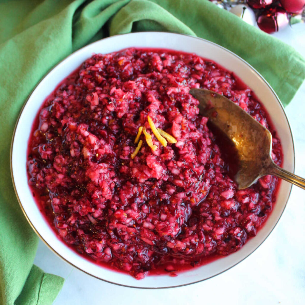 Serving bowl of orange cranberry relish with orange zest and serving spoon.