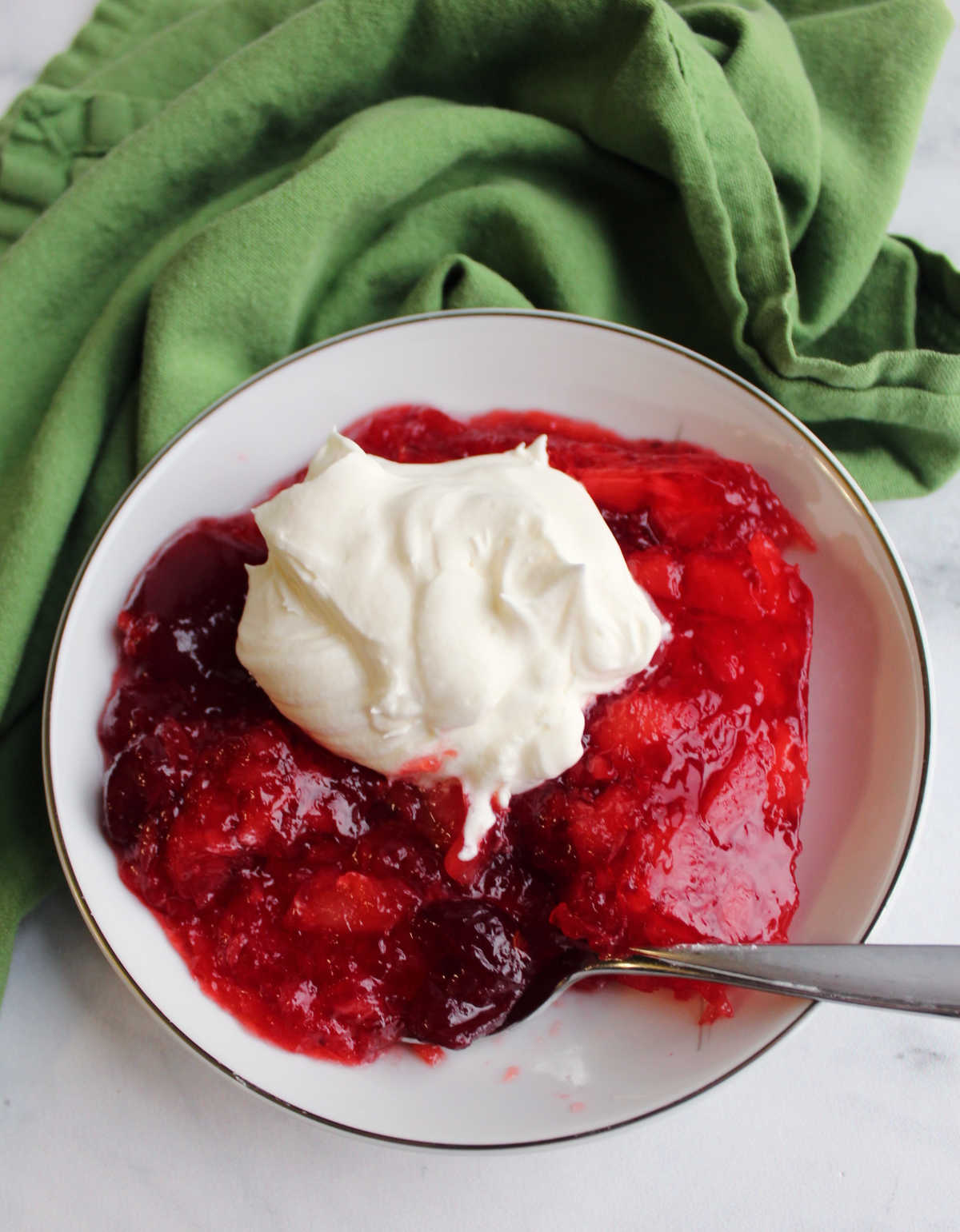 Small bowl of cranberry jello salad with a dollop of fresh whipped cream on top.